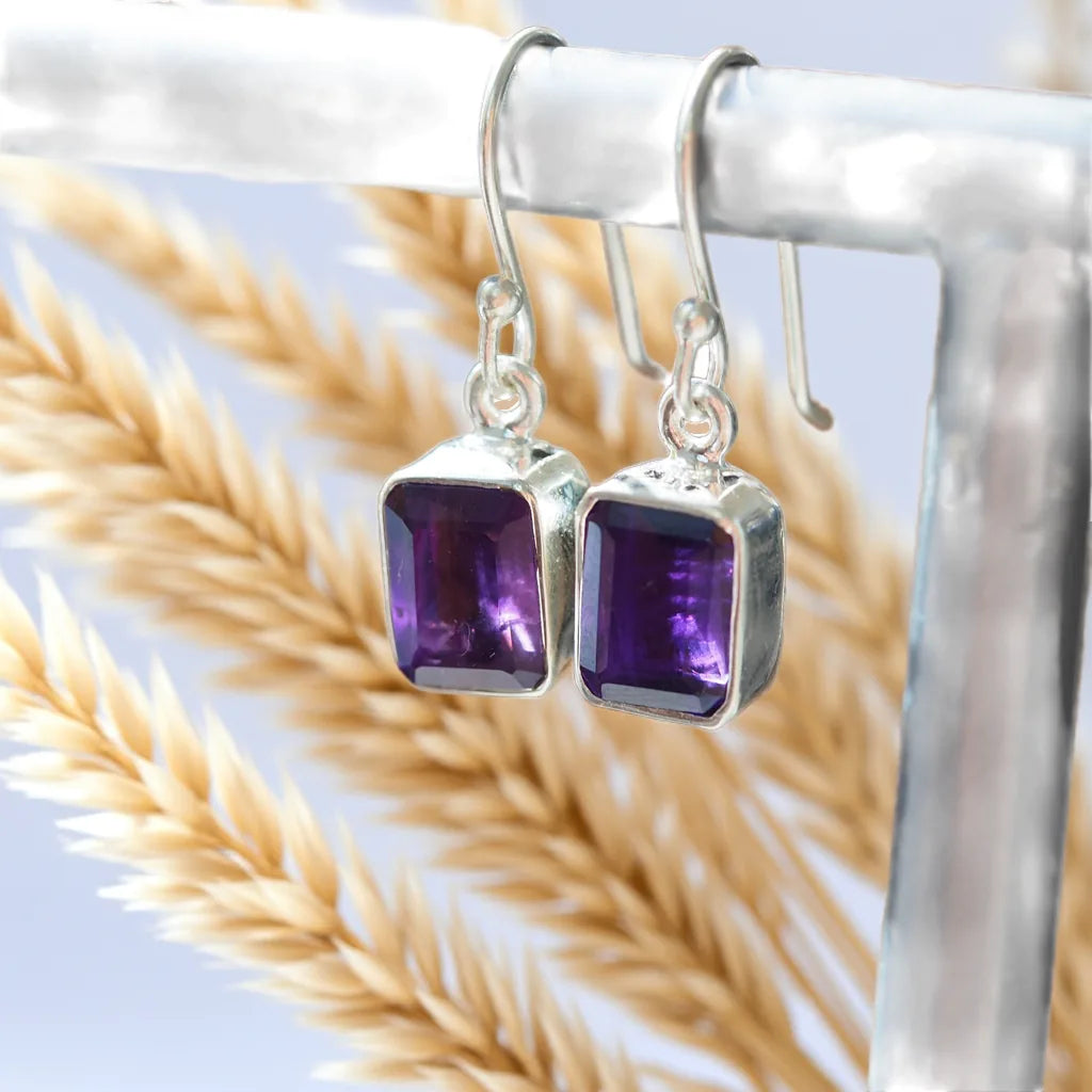 Silver earrings with purple gemstones on a light background