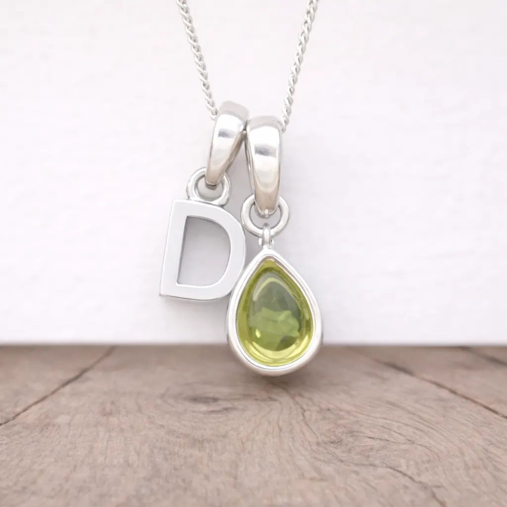 Silver necklace with a 'D' pendant and a teardrop-shaped green gemstone on a wooden surface.