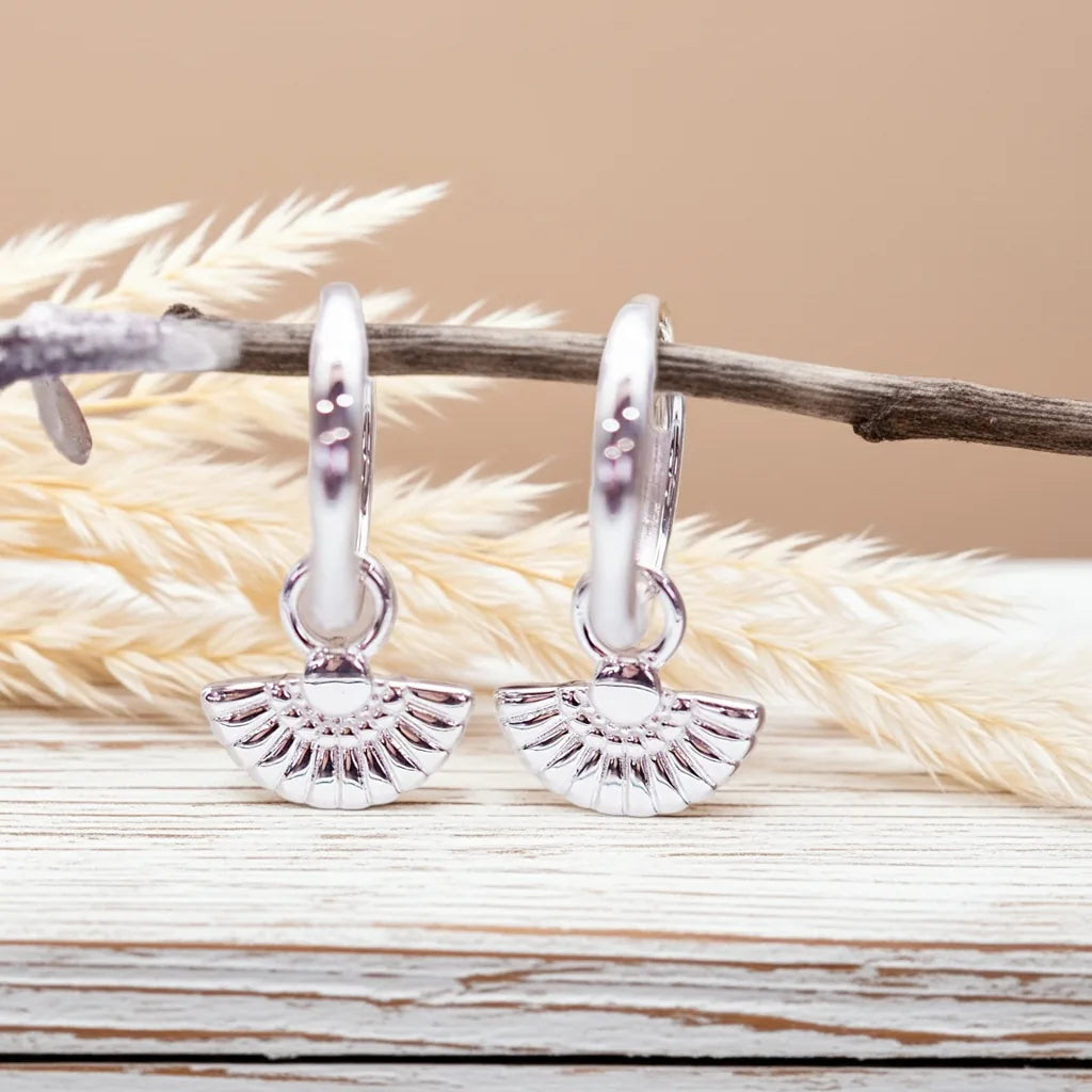 Silver hoop earrings with a textured design on a wooden surface with dried grass.