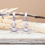 Silver hoop earrings with a textured design on a wooden surface with dried grass.