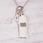 Silver necklace with 'A' pendant and Aquarius symbol on a light wooden background