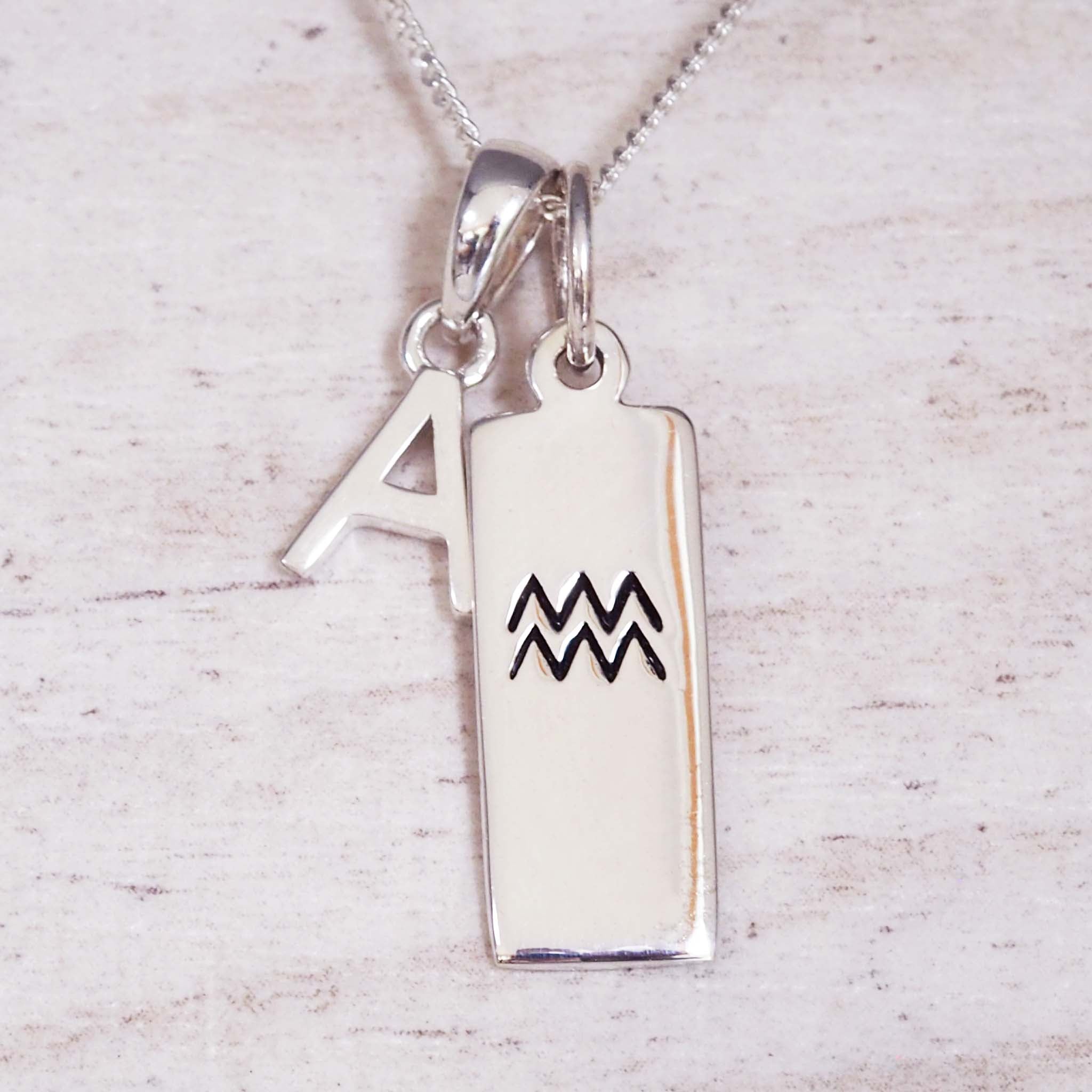 Silver necklace with 'A' pendant and Aquarius zodiac symbol pendant on a light wooden background