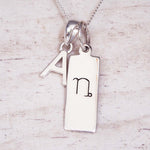 Silver necklace with a pendant featuring the letter 'A' and a symbol on a light wooden background