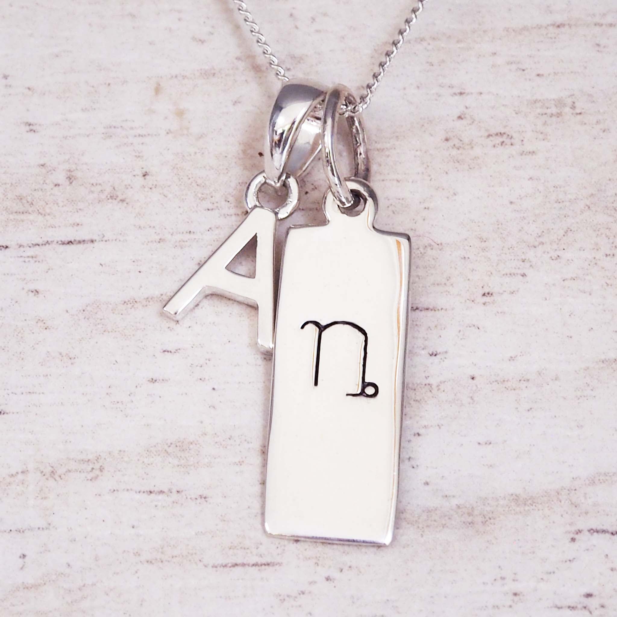 Silver necklace with a pendant featuring the letter 'A' and a symbol on a light wooden background