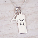 Silver necklace with a rectangular pendant featuring a black astrological symbol and a letter 'A'.