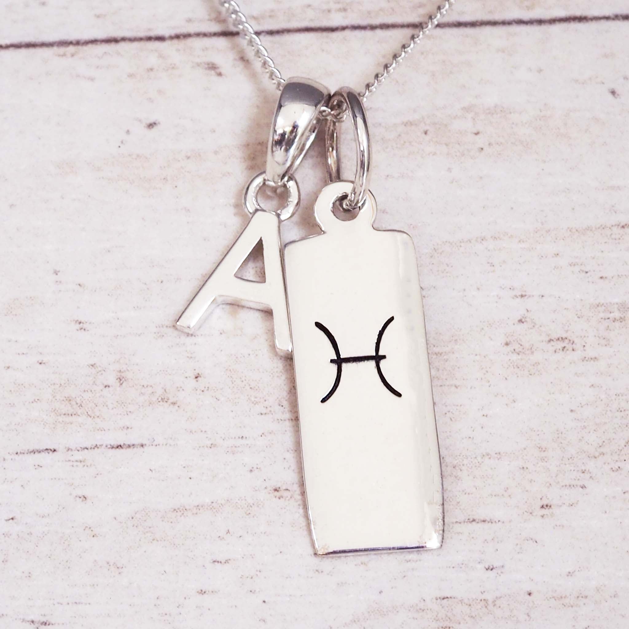 Sterling Silver Pisces Zodiac necklace with a letter 'A' charm on a light wooden background
