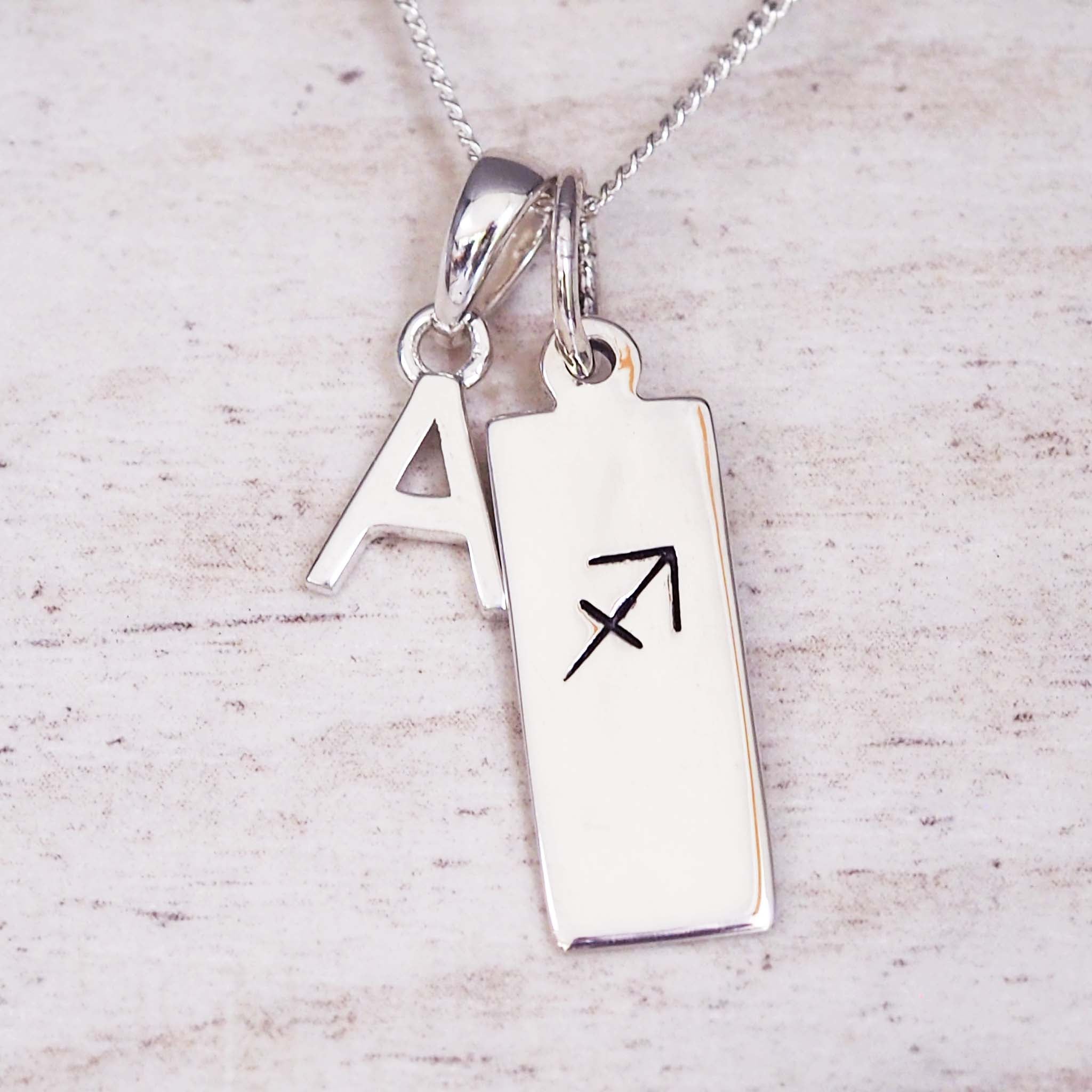 Silver necklace with a pendant featuring an 'A' and a sagittarius symbol on a light background