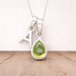 Silver necklace with a green teardrop pendant on a wooden surface