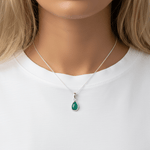 Silver necklace with tear drop emerald stone being worn by woman with blonde hair and a white tee 