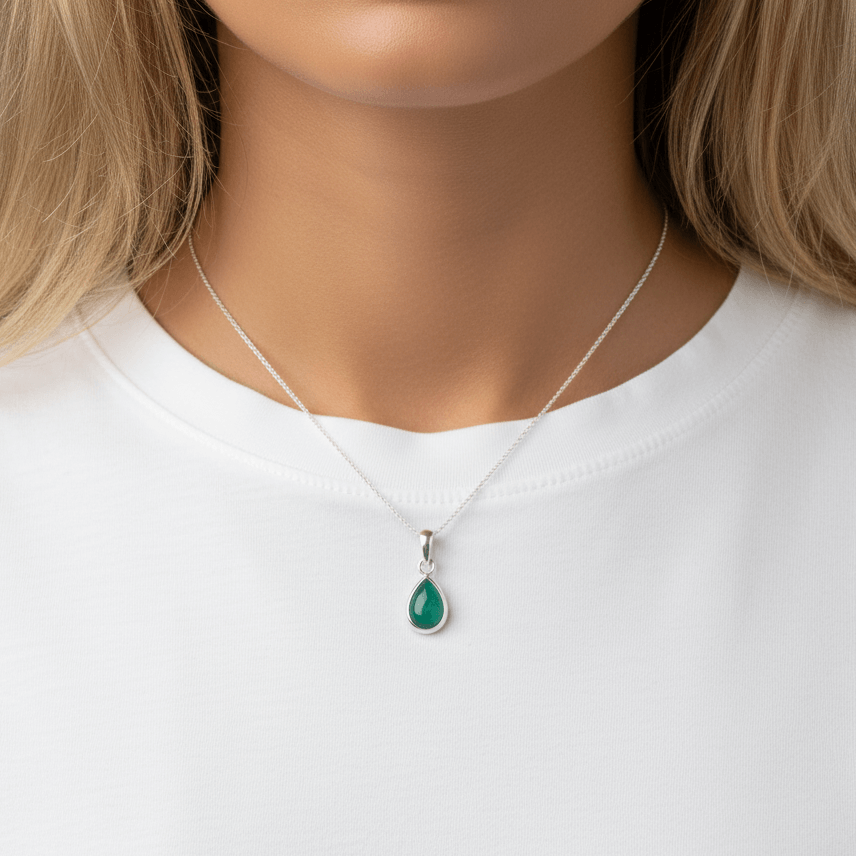 Silver necklace with tear drop emerald stone being worn by woman with blonde hair and a white tee 
