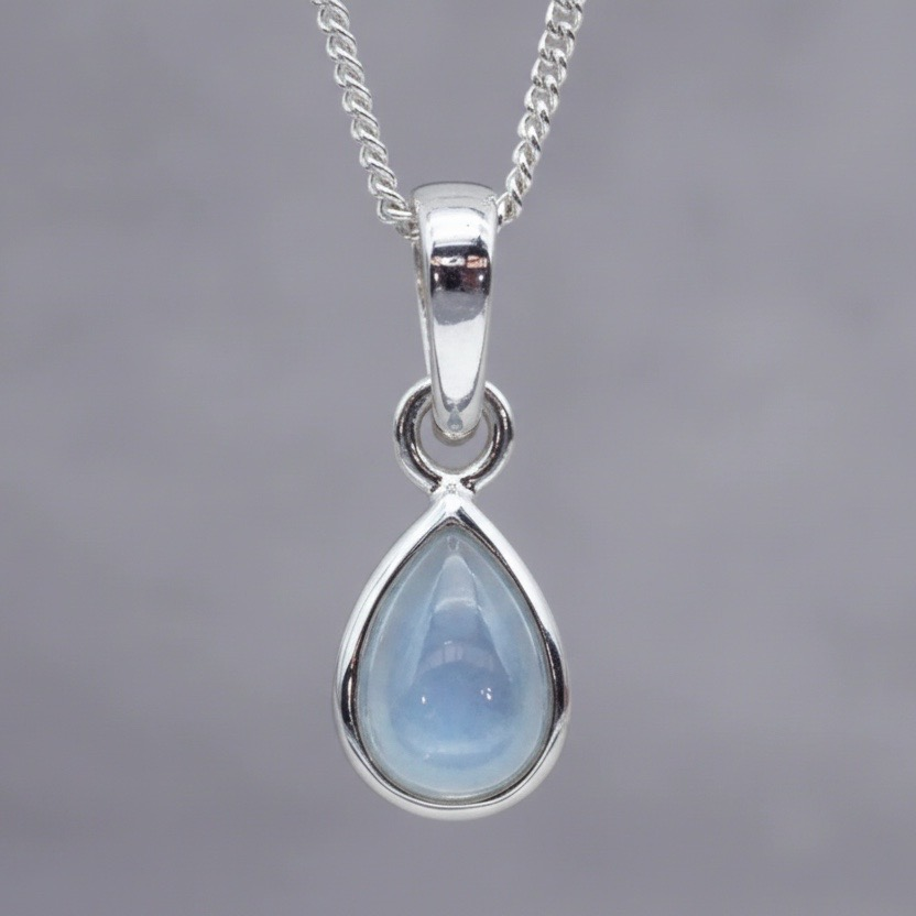 Teardrop-shaped pendant with blue topaz stone on a silver chain against a gray background