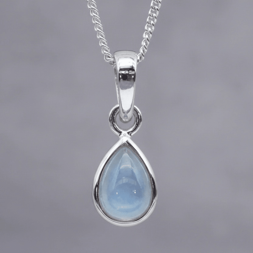Teardrop-shaped pendant with blue topaz stone on a silver chain against a gray background