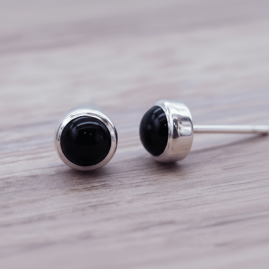 Pair of black onyx stud earrings with silver posts on a wooden surface