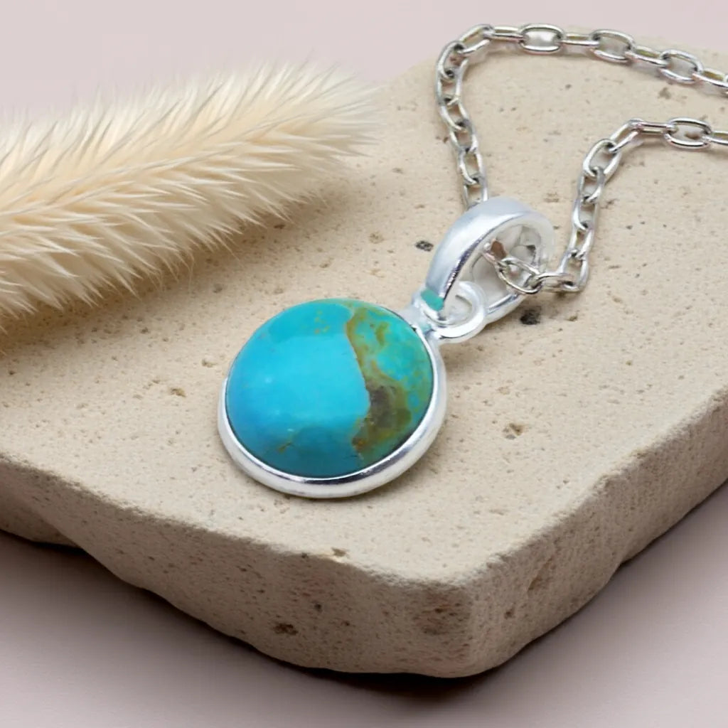 Turquoise pendant necklace on a textured surface with dried grass