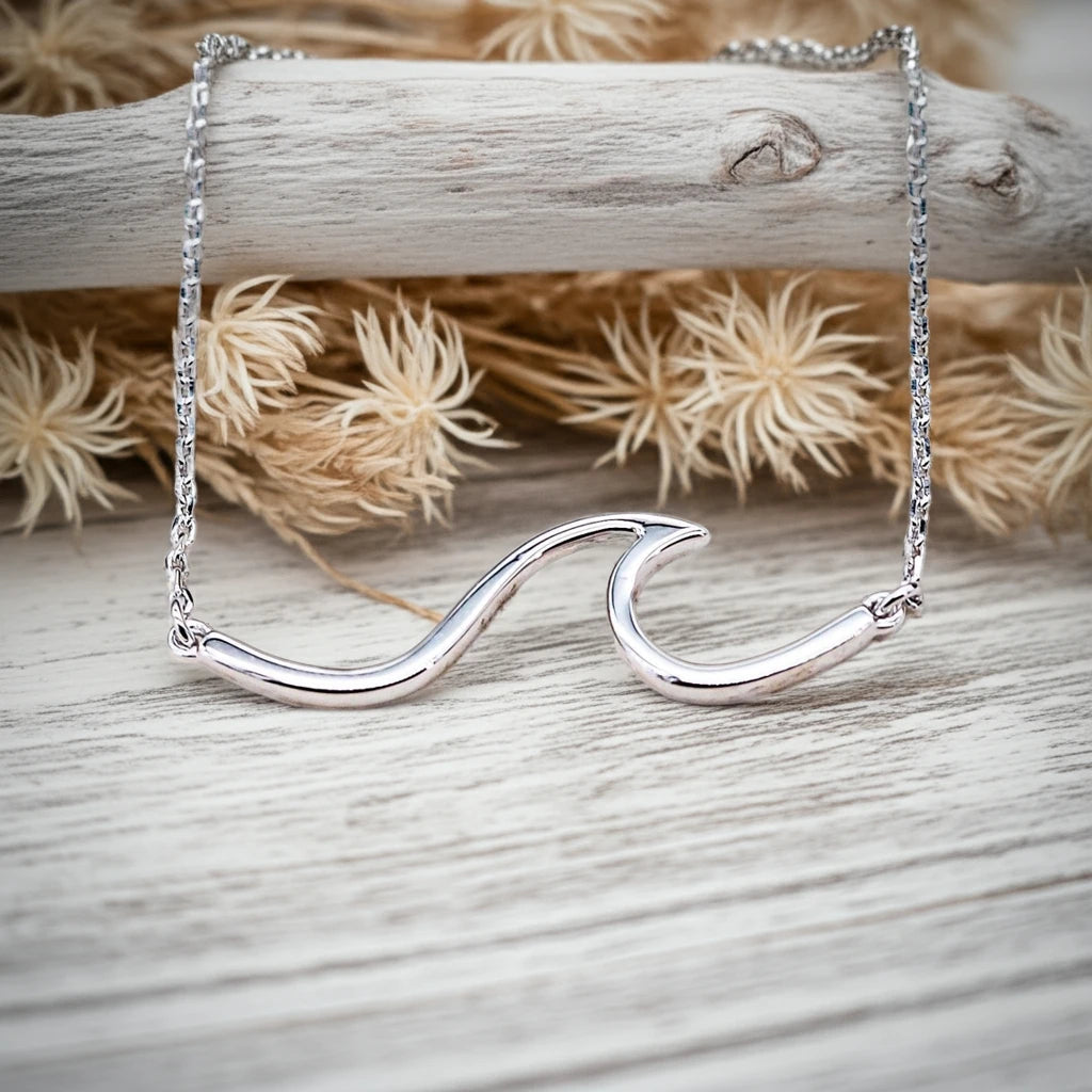 sterling Silver wave-shaped necklace on a wooden surface with dried flowers in the background by indie and harper australia