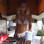 Woman in a bikini inside a van with a red teapot and floral decorations.