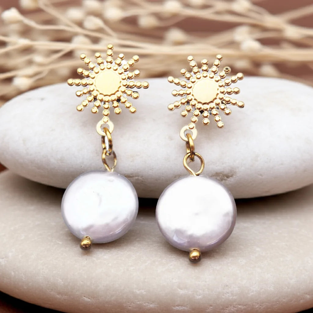 Gold sun-shaped earrings with pearl drops on a stone surface