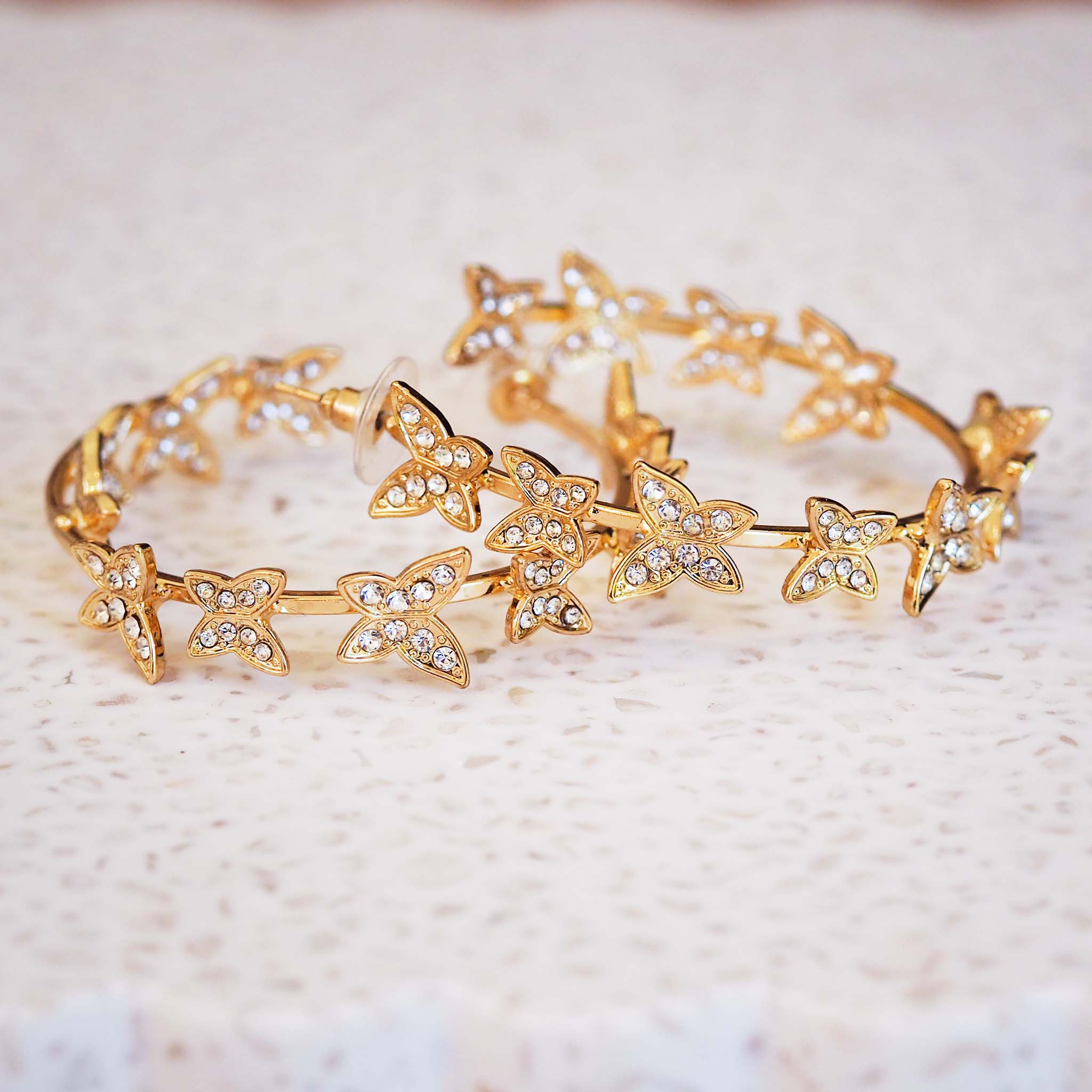 Gold hoop earrings with butterfly designs on a light background