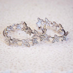 Silver earrings with butterfly-shaped charms on a textured beige background