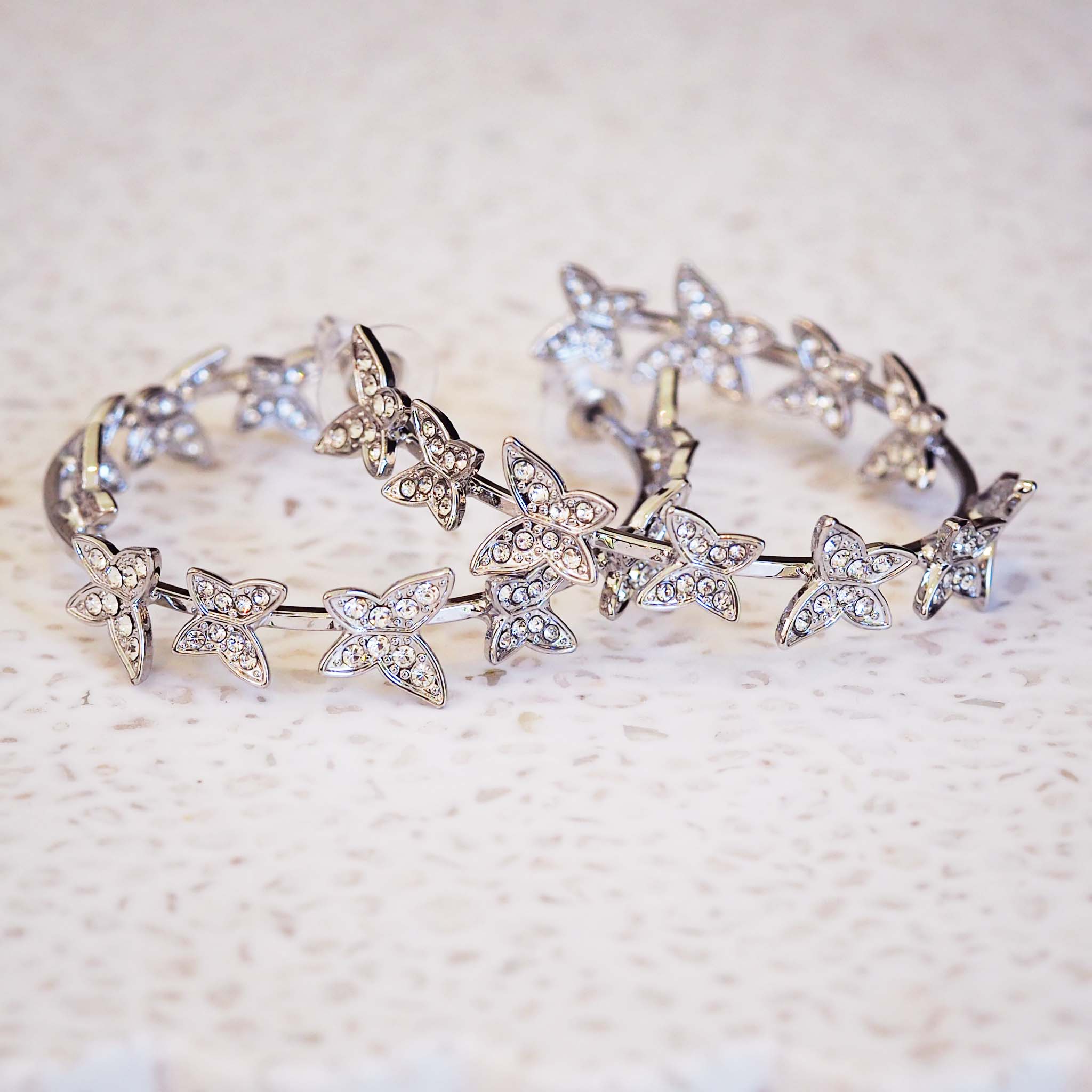 Silver earrings with butterfly-shaped charms on a textured beige background