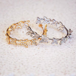Two butterfly-shaped earrings on a textured beige surface