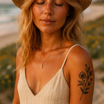 Woman with a tattoo on her arm wearing a beige dress, silver citrine necklace and straw hat outdoors.