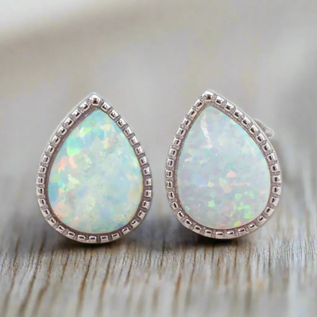 Teardrop-shaped opal earrings with silver frames on a wooden surface.