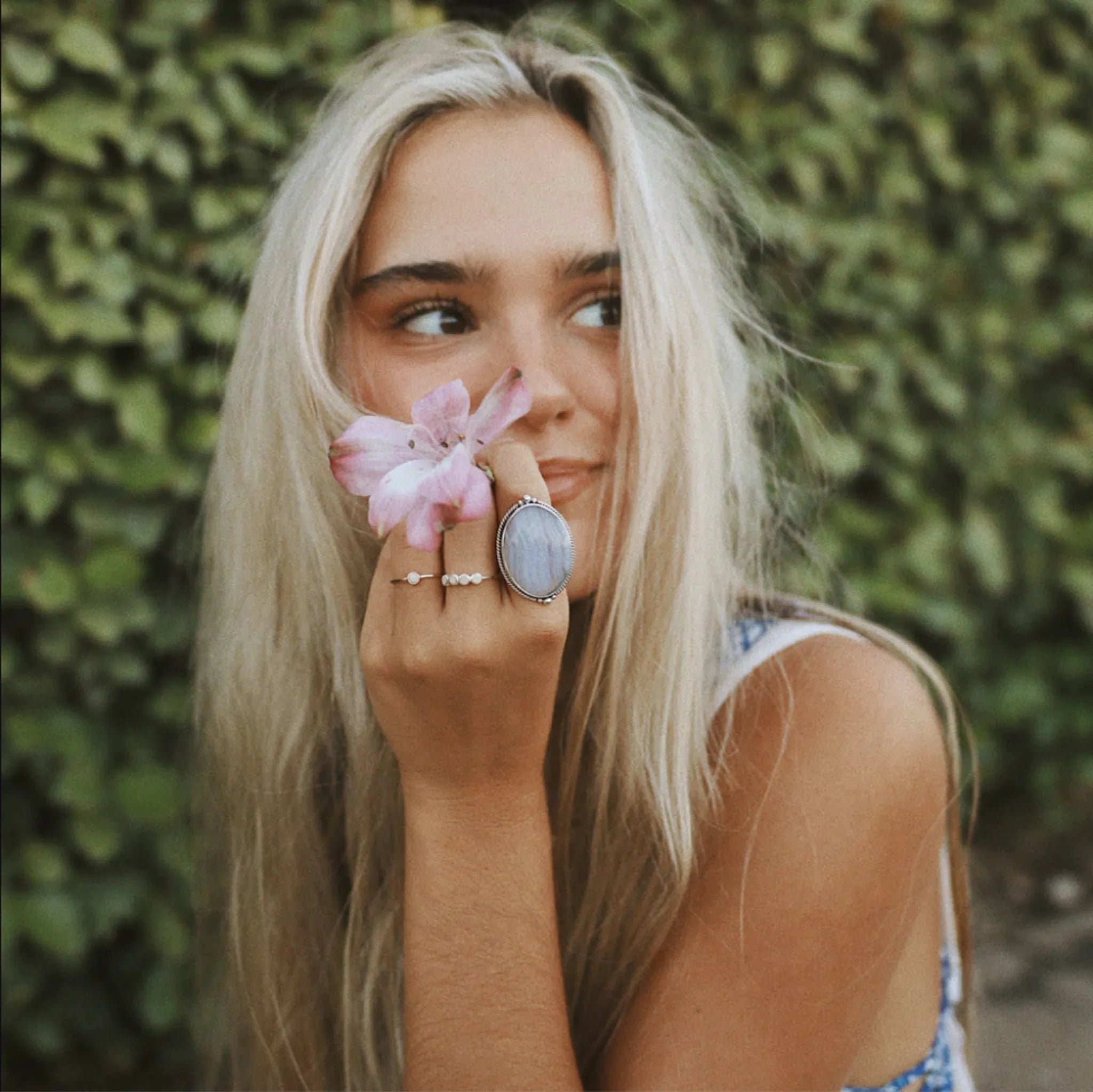 girl with blonde hair holding a flower and wearing boho rings