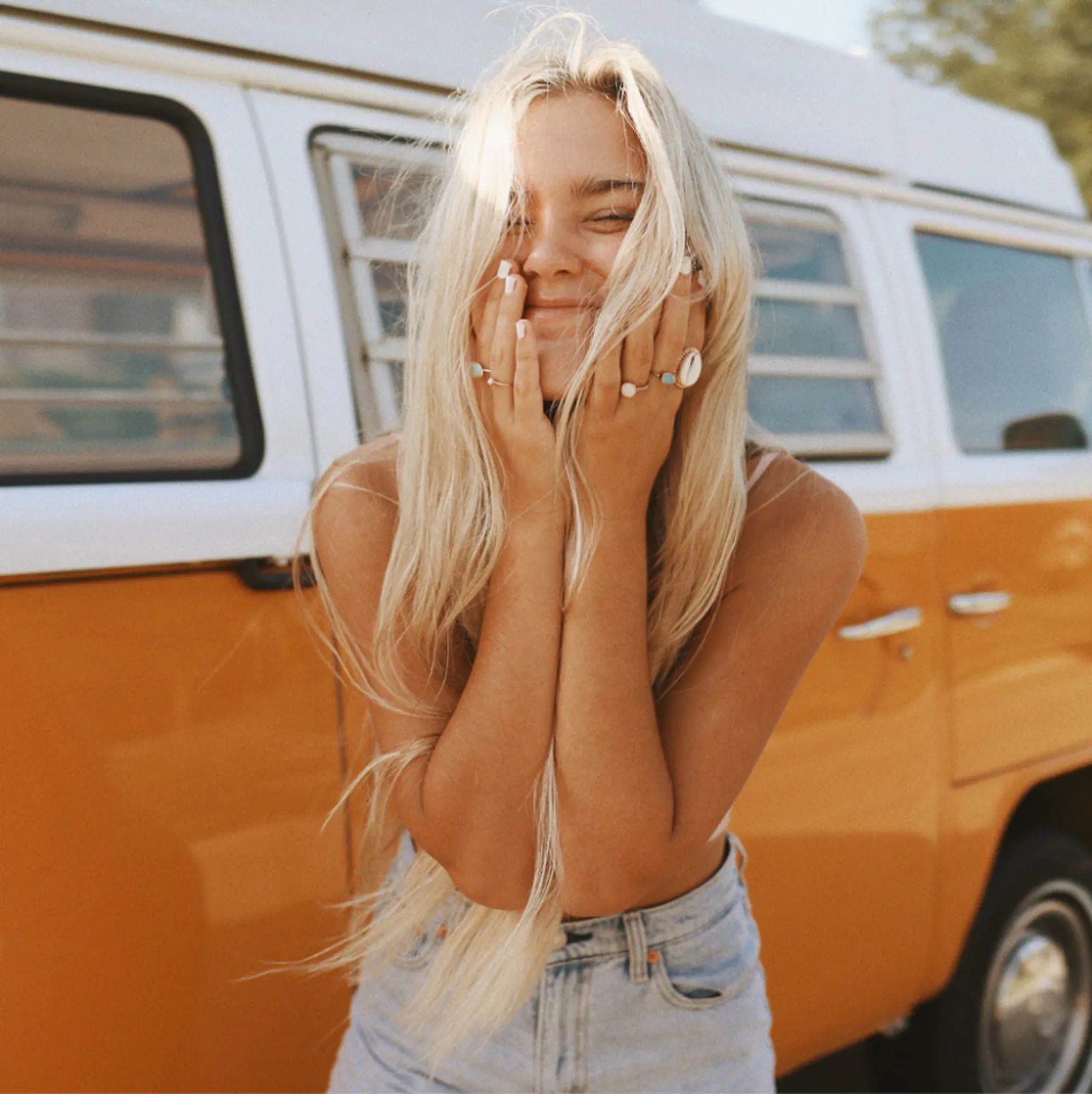 smiling girl in front of a orange combi van, smiling and wearing boho jewellery