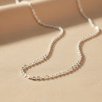 close up of a dainty italian sterling silver fine chain anklet laying on a light surface