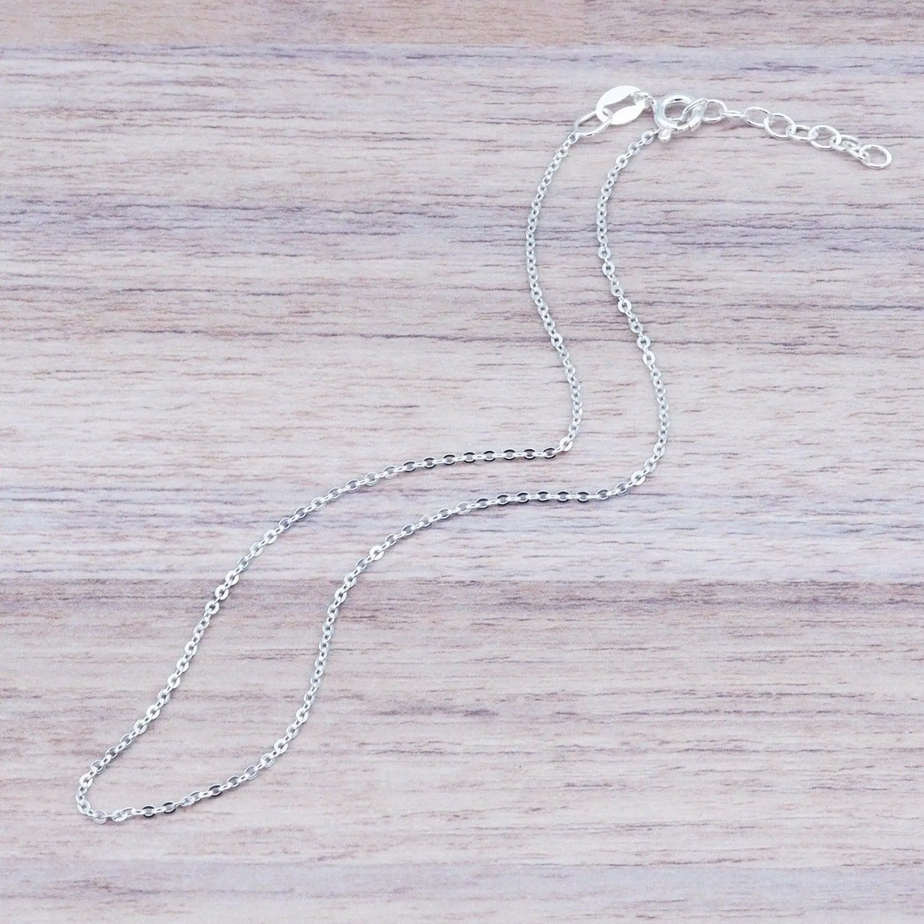 dainty italian sterling silver fine chain anklet laying on a light wooden surface