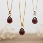 Three teardrop-shaped gemstone garnet pendants on chains against a beige background.