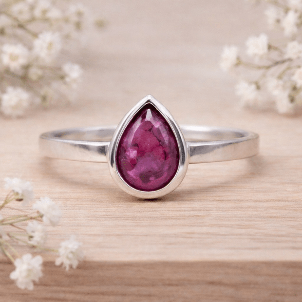 Silver ring with a teardrop-shaped ruby stone on a wooden surface