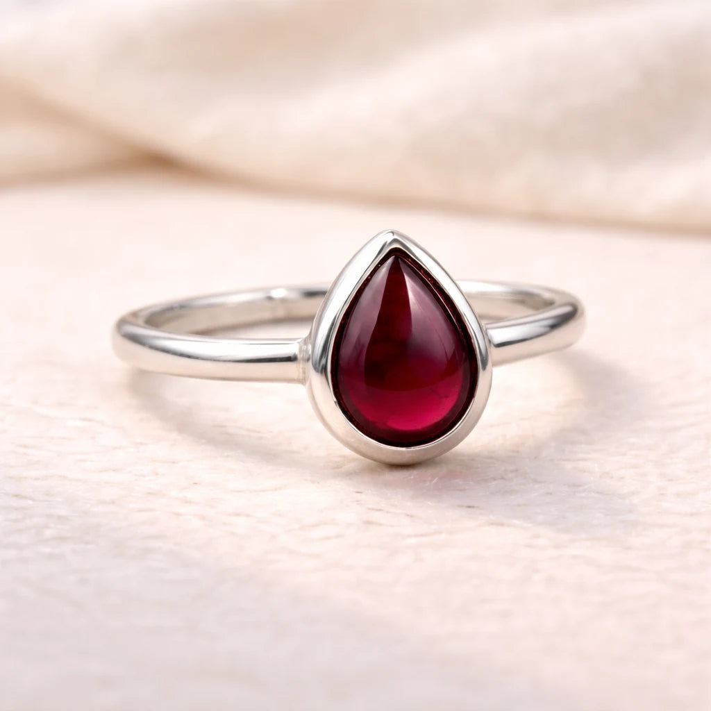 Silver ring with a red teardrop-shaped gemstone on a soft beige background