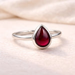 Silver ring with a red teardrop-shaped gemstone on a soft beige background