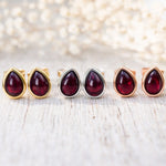 Set of teardrop-shaped gemstone earrings in gold, silver, and rose gold on a light background.