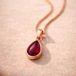 Rose gold January Birthstone necklace with a red teardrop natural garnet gemstone pendant on a beige background