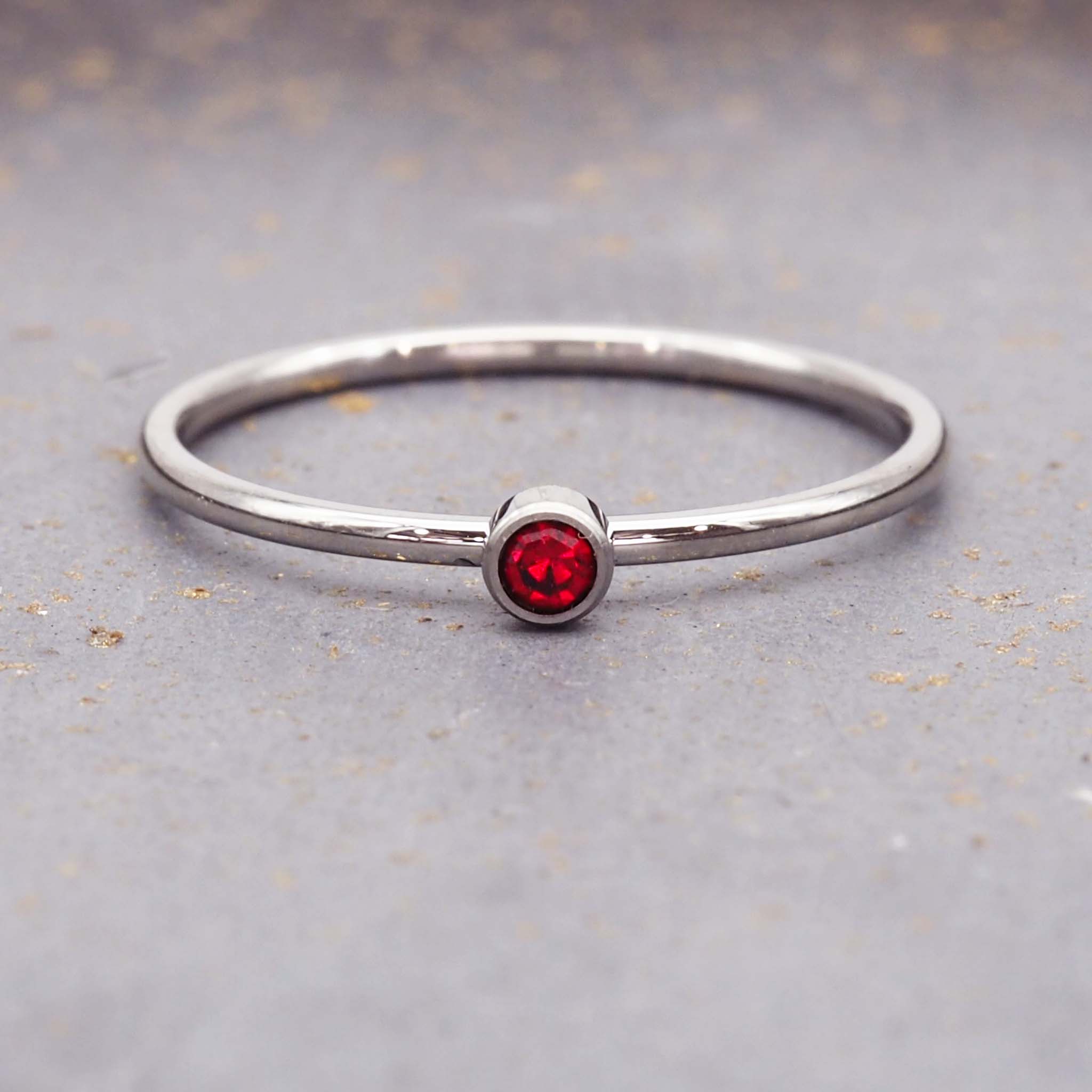 Dainty silver stacker ring featuring a round red cubic zirconia stone on a polished stainless steel band.