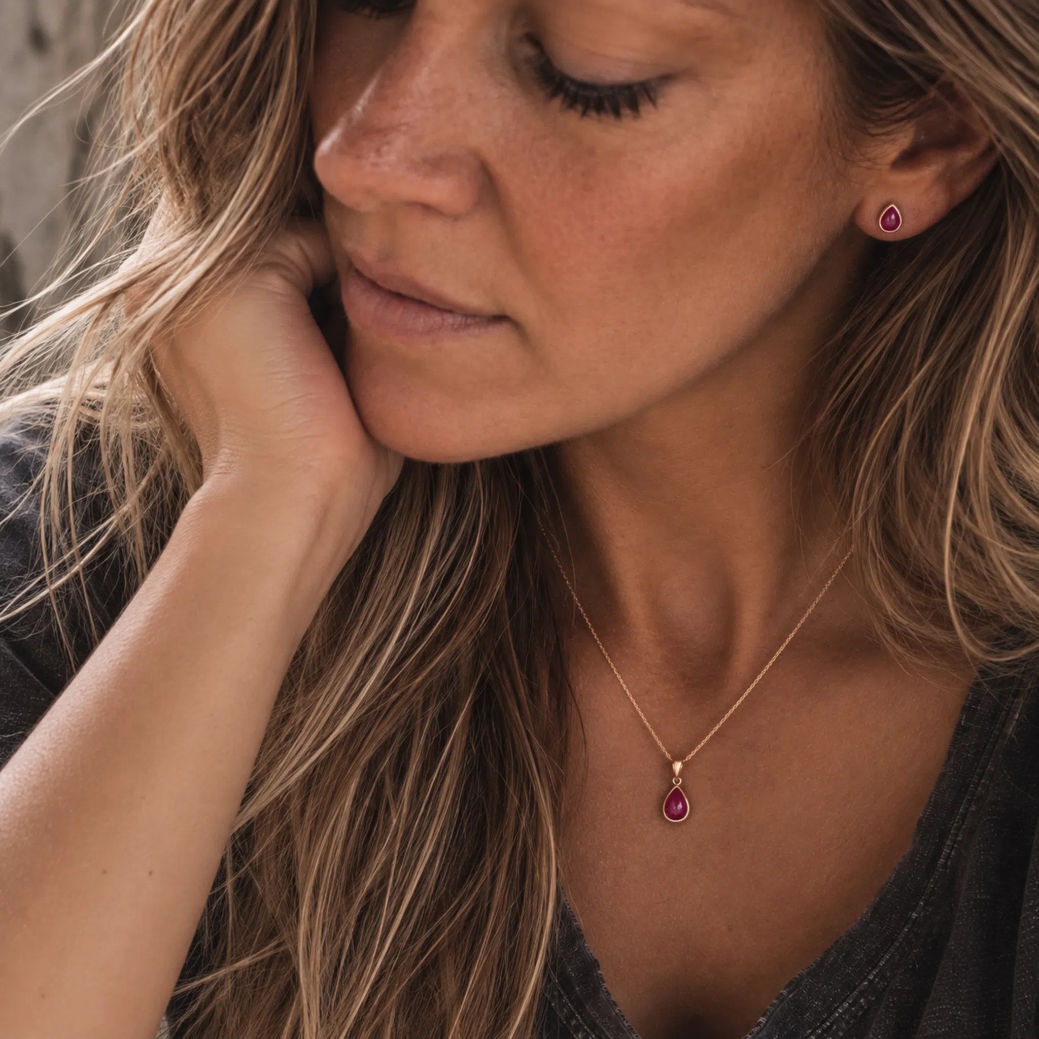 A close-up of a model wearing the gold July Birthstone Jewellery Set featuring the matching teardrop pendant natural ruby necklace and stud ruby earrings.