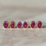 Three Pair of tear drop stud earrings in rose fold, silver and gold with red ruby gemstones on a beige background