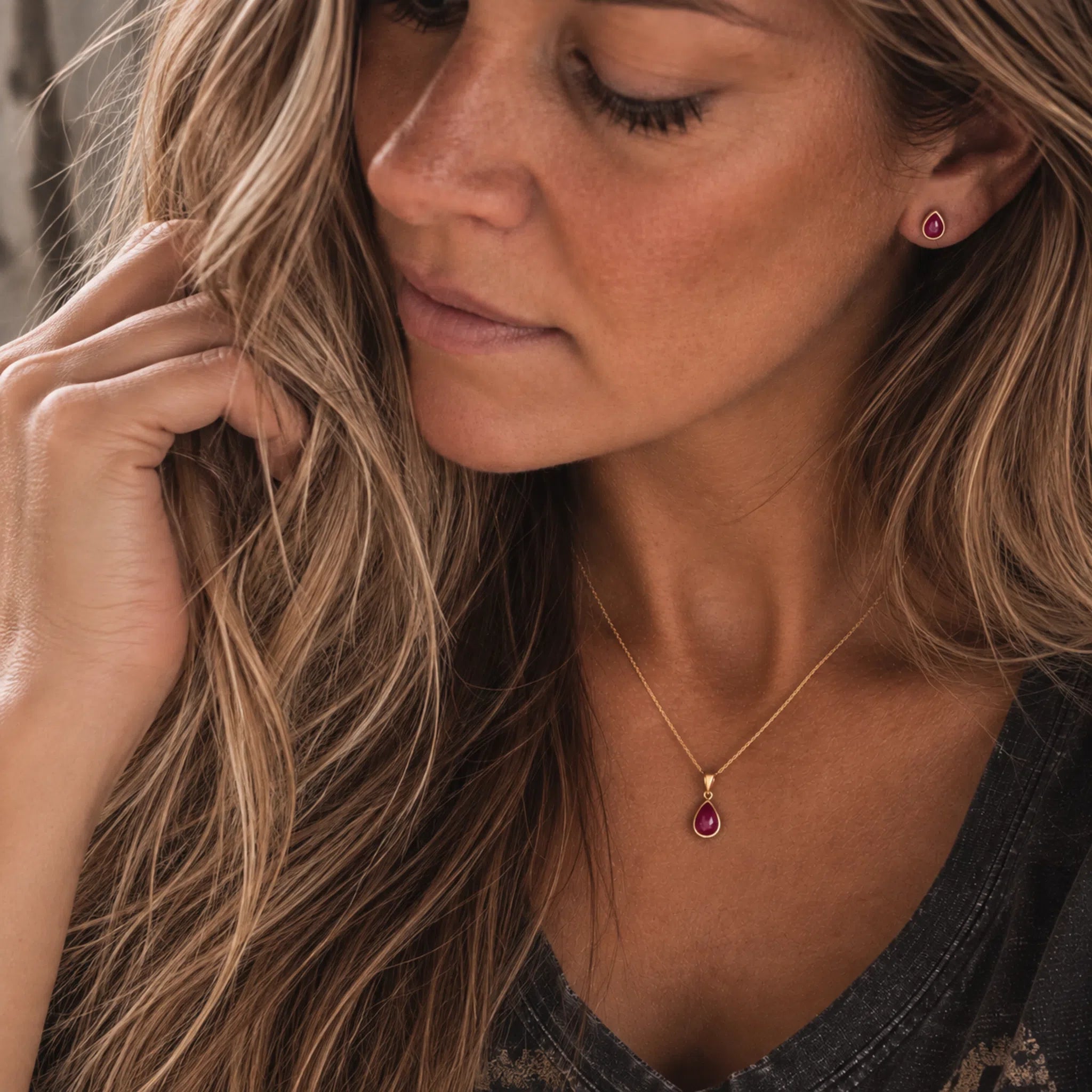 A close-up lifestyle shot of a woman wearing july birthstone jewellery set featuring a delicate gold chain necklace with a small teardrop-shaped natural ruby pendant, along with matching stud ruby earrings.