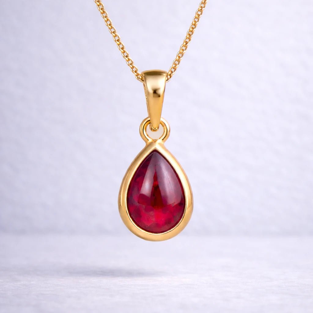 Gold necklace with a red teardrop natural ruby gemstone pendant on a white background