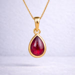 Gold necklace with a red teardrop natural ruby gemstone pendant on a white background