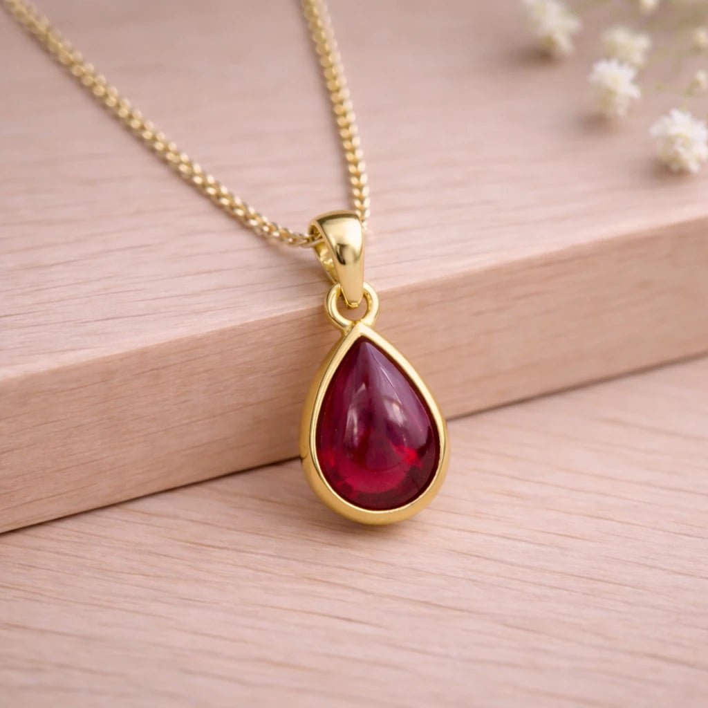 Gold necklace with a red teardrop natural ruby gemstone pendant on a wooden background