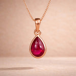 rose Gold necklace with a red teardrop natural ruby gemstone pendant on a beige background