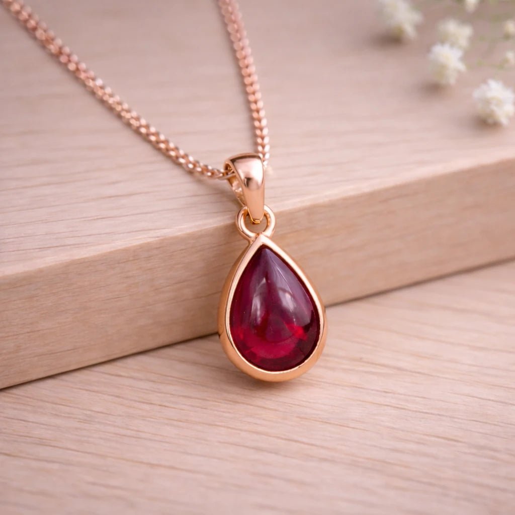 Rose Gold necklace with a red teardrop natural ruby gemstone pendant on a wooden background