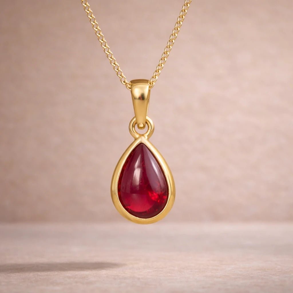 Gold necklace with a red teardrop natural ruby gemstone pendant on a beige background