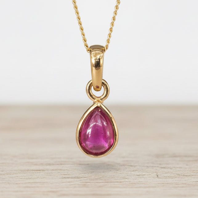Gold pendant with a ruby gemstone on a light wooden surface