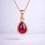 Rose gold necklace with a red teardrop natural ruby gemstone pendant on a light gray background