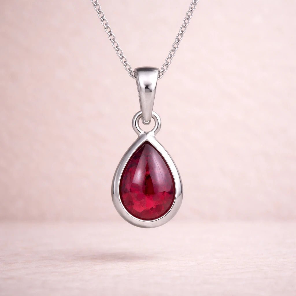 Sterling Silver necklace with a red natural ruby gemstone teardrop shaped pendant on a beige background